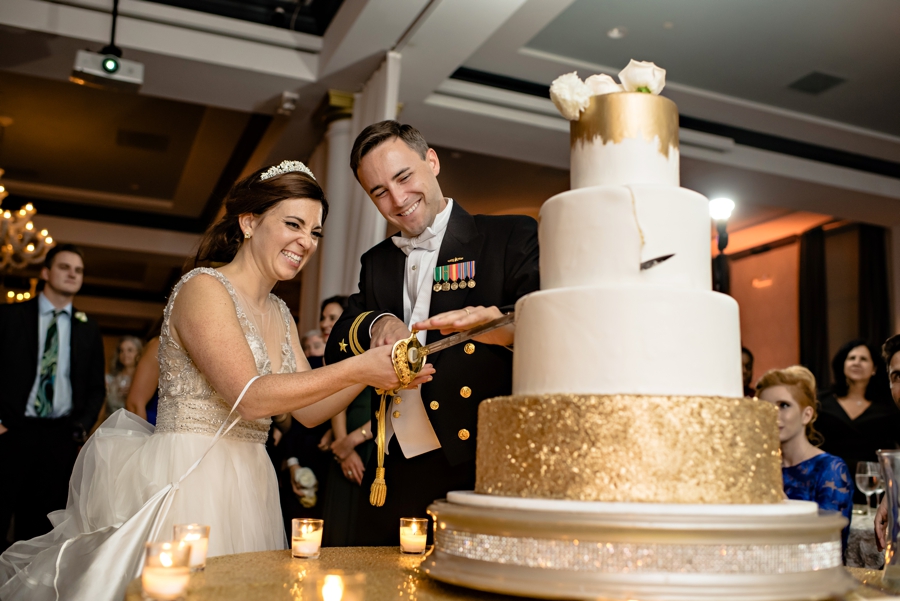 A wedding couple cut the wedding cake with a Navy sword.